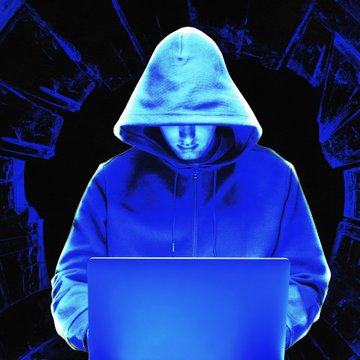 A hooded figure types on a laptop bathed in blue light, symbolizing the cyber thief who stole over $4.8 million in bitcoin from a task scammer's tampered Ledger wallets.