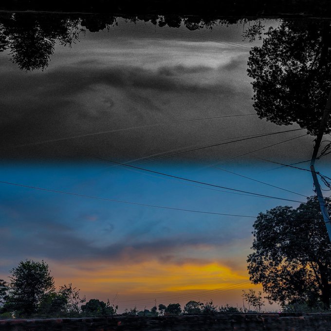 A surreal mirrored sunset sky over a rural landscape with power lines and silhouetted trees, evoking the otherworldly atmosphere fitting for a call to support artists in the #AEW Tezos community. The split composition, with its vivid orange horizon meeting an inverted dark cloudscape above, symbolizes the dual nature of creative support—grounded reality and boundless imagination.