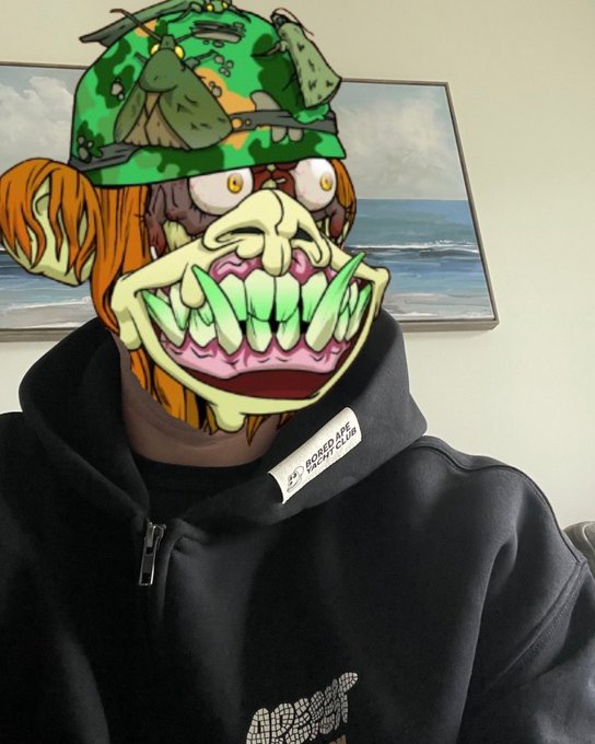 A person wears a vibrant Bored Ape NFT mask featuring a camo hat and green teeth, paired with a black hoodie bearing a "Bored Ape" label—visually embodying pride and membership in the Bored Ape Yacht Club community.