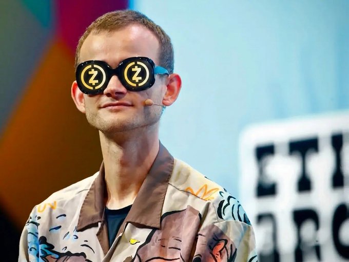 A man stands on a stage wearing a jacket with colorful patterns and large, round sunglasses featuring a "Z" symbol.