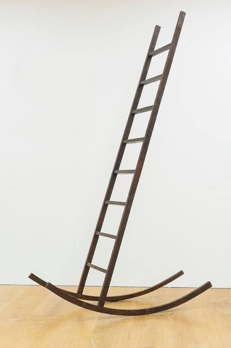 An art installation featuring a wooden ladder mounted on curved rockers resembling a rocking chair base, displayed in a gallery setting.