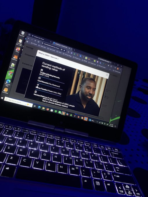 A laptop displays a webpage titled 'What is USDC? | Episode 2' showing 'Current methods of sending value' including USDC, ACH, and Mastercard, alongside a video of a man.