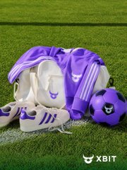 A purple soccer/football uniform set including jersey, shorts, and a soccer ball branded with the "XBIT" logo rests on a green field. The caption relates to the post's reference to the World Cup and sports betting, with "XBIT" being the platform mentioned in the accompanying text.