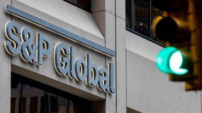 An exterior sign displays "S&P Global" in large illuminated lettering on a building facade. The image visually reinforces the article's mention of S&P Global Ratings launching a new risk assessment framework for on-chain lending vaults, with a green traffic light visible in the foreground.