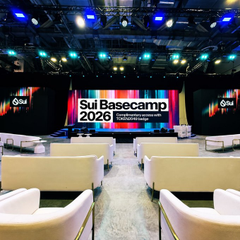 An empty conference venue is set up for 'Sui Basecamp 2026,' featuring rows of white cushioned chairs facing a stage with Sui branding and blue lighting overhead.