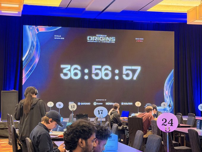 A conference room at 'TOKEN2049 ORIGINS' in Singapore showing a countdown timer at 36:56:57, supported by Cardano, Chainalysis, Robinhood, and Solayer.