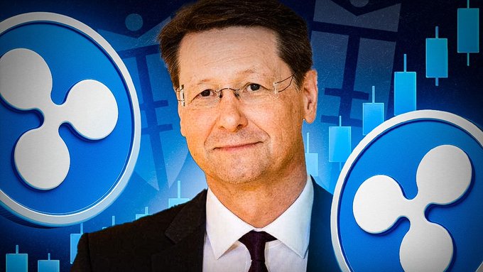 A professional man in a dark suit, white shirt, and dark tie with glasses stands in front of a blue background featuring the XRP cryptocurrency logo and candlestick chart graphics, visually reinforcing the article's discussion of Michael Oliver's bullish forecast for XRP's role in the future financial system.