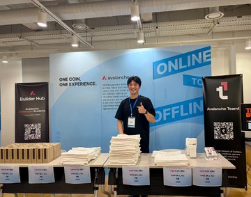 A man stands at a trade show booth for Avalanche with the slogan 'ONE CORE, ONE EXPERIENCE,' displaying merchandise on a table beneath banners reading 'ONLINE TO OFFLINE' and 'Builder Hub Avalanche Team.'