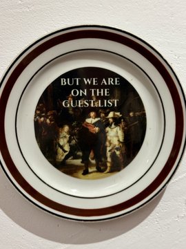A decorative ceramic plate with maroon stripes features a vintage illustration and the text 'BUT WE ARE ON THE GUESTLIST'.