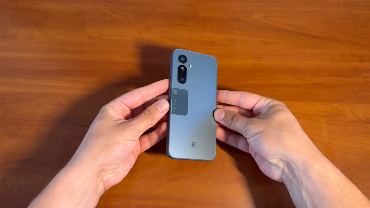 The image shows a person holding up an old cell phone, possibly a flip phone or a small smartphone with a camera lens attachment, over their head as if they are showing off its features. The photo appears to be taken at a wooden table, which adds a rustic touch to the scene. The post seems to be related to the cell phone, possibly discussing its history or showcasing it for sale.