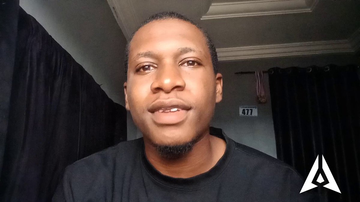 The image features a man wearing a black shirt, with his face turned towards the camera. The background of the photo shows a dark room or hallway, which contrasts with the man's attire. There are no texts or other objects present in the image.