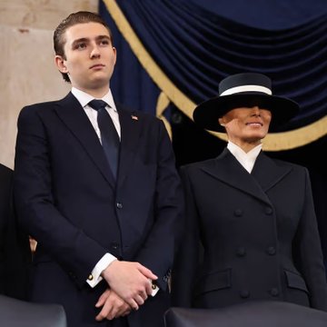 Barron Trump, dressed in a sharp navy suit and tie, stands beside his mother Melania Trump, who wears a wide-brimmed black hat and tailored black coat, at what appears to be a formal political event. The image accompanies news that the 20-year-old Barron has reportedly amassed a $150 million fortune through his stake in the family's World Liberty Financial crypto venture, eclipsing his mother's wealth.