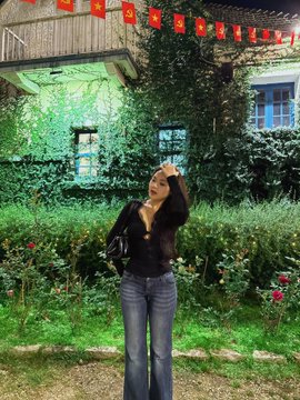 A woman stands smiling in front of an ivy-covered building lit up with red banners, posing to celebrate her new deal. The setting suggests a milestone moment, aligning with her excitement about being backed by YZi Labs (Hertzflow_xyz).