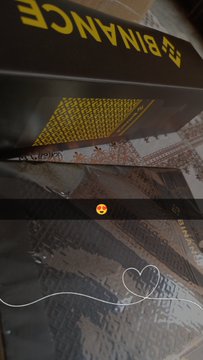 Movie poster or promotional image showing the word 'BINANCE' in yellow letters at the top, with a small orange smiley face emoji and faint sketches visible on the dark surface below.