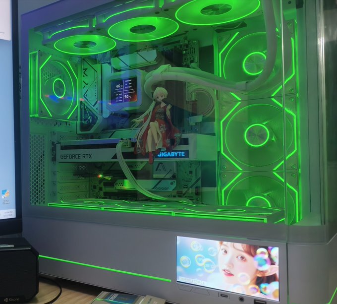 A custom gaming PC setup featuring a Gigabyte GeForce RTX graphics card, illuminated with bright green RGB fans, and decorated with an anime figurine inside the transparent case.
