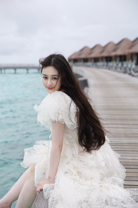 A young woman with long dark hair sits on a wooden boardwalk over the ocean, wearing a flowing white polka-dot dress and glancing over her shoulder with a soft smile, while overwater bungalows line the pier in the background. The serene, elegant image suggests a peaceful moment of personal reflection, visually echoing her message about taking time to pause after leaving OKX and considering her next career step.

Note: There is no visible text, numbers, tickers, or names in the image itself.