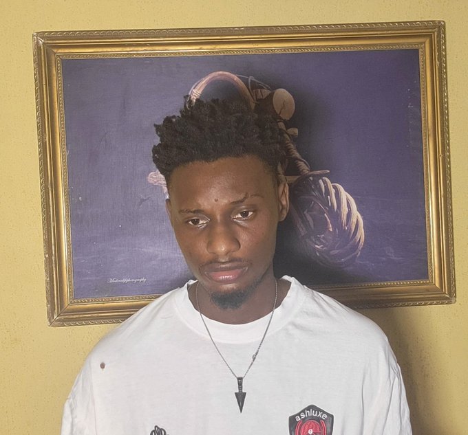 A young man with short locs stands before a framed classical painting featuring a vintage figure with headphones, wearing a white t-shirt and a triangular pendant. His serious, contemplative expression mirrors the romantic weight of the caption about mutual appreciation and valuing one another.