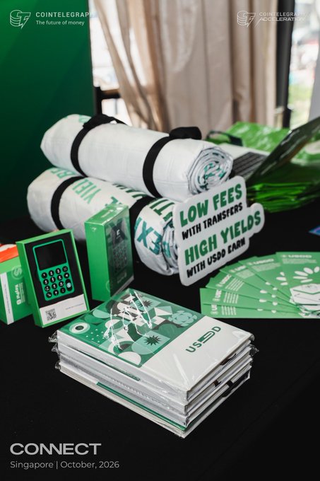 A promotional image for 'Cointelegraph The future of money' CONNECT event in Singapore, October 2026, featuring rolled-up white towels with green text reading 'LOW FEES WITH TRANSFERS, HIGH YIELDS WITH USDC EARN', alongside green merchandise and promotional materials.