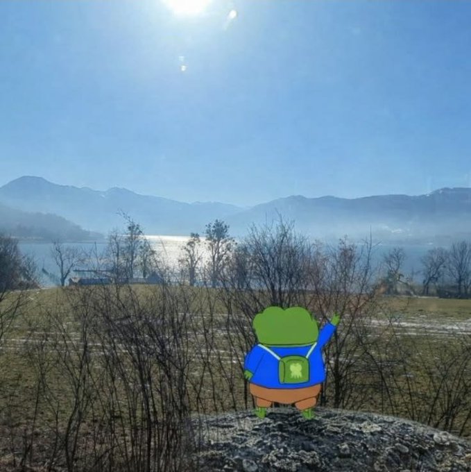 An animated illustration of a frog character wearing a blue outfit and green backpack standing on a rock, overlooking a misty lake with mountains and a bright sun overhead.