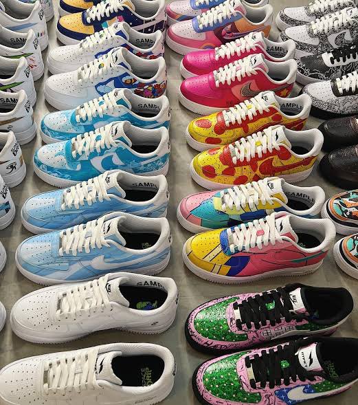 An overhead view of numerous colorful custom Nike Air Force 1 sneakers, some labeled 'SAMPLE', arranged in rows displaying various artistic designs.