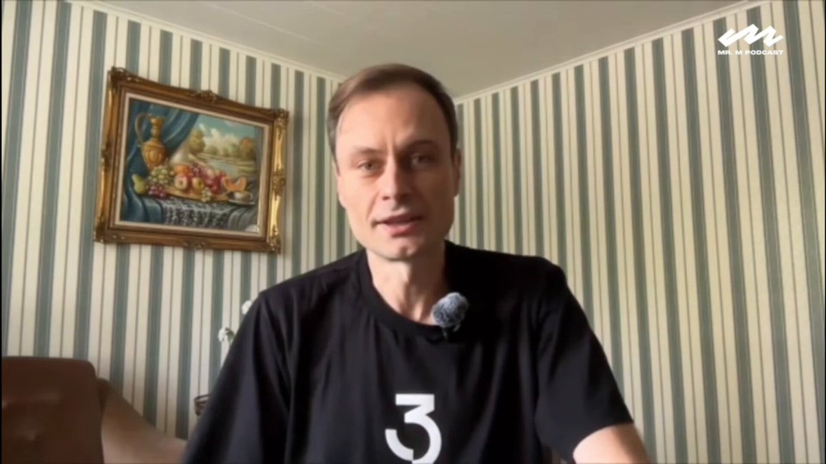 The image shows a man wearing a black t-shirt with the number 3 printed on it. He appears to be sitting at a desk or table while talking into a microphone, possibly participating in an online meeting or event. The background features a striped wall that adds visual interest to the scene. The post includes text about Bitcoin and a link to a Bitcoin news site, suggesting that the man might be discussing or sharing information related to this digital currency.