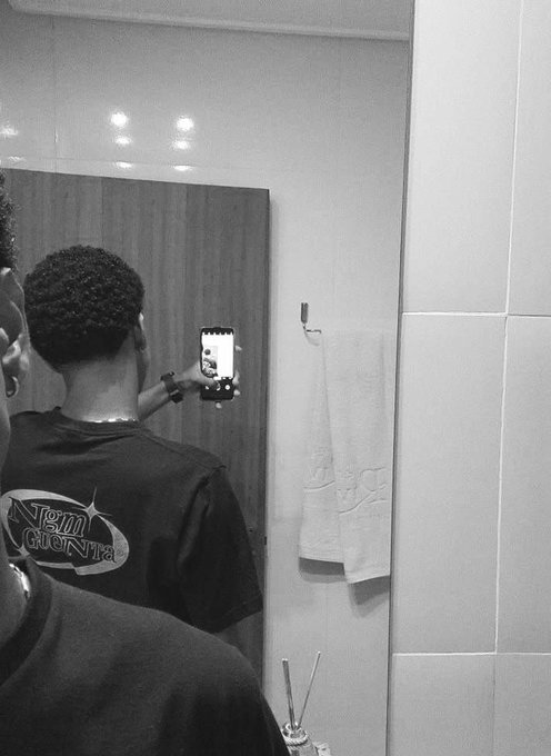 A black and white photo of a person in a Team Gonza shirt taking a mirror selfie with their phone.