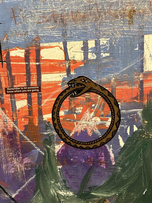 An artistic mixed-media piece featuring a snake biting its own tail (ouroboros) on a textured background, with a small label reading 'Remember to let someone know where you are going.'
