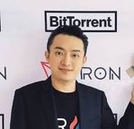 A man in a black blazer and t-shirt stands in front of a white backdrop featuring the 'BitTorrent' logo.