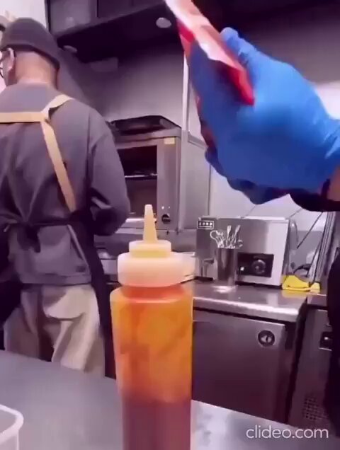 The image shows a man wearing blue gloves holding a red bottle of ketchup, which appears to be a bottle of hot sauce or mustard. There are two other people present in the scene - one person standing behind the man with the ketchup bottle and another person sitting at a table nearby. The background features an oven and a microwave, suggesting that they might be in a kitchen setting.

The image also contains text that reads "This is how bitcoin transactions work". This could be related to the ketchup bottle or some other object within the scene, but it's unclear what specific connection there is between the ketchup bottle and Bitcoin transactions.