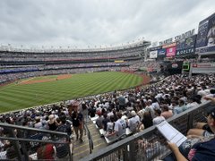 A view from the upper deck of Yankee Stadium looking down at the baseball field and crowd under a partly cloudy sky.