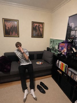This image shows a young man posing on a couch with a plate of food, offering the best caption for 1 SOL. Perhaps he's waiting to see which of his possessions, pictured on the shelves, inspired the winning caption.