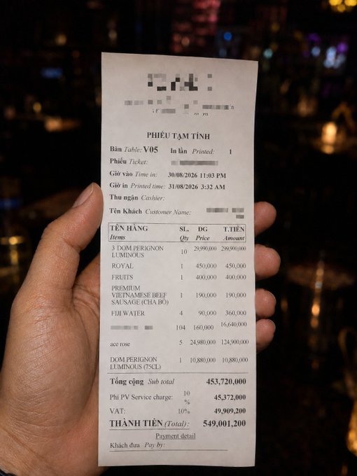 A hand holds a Vietnamese restaurant receipt from V05 dated 31/08/2026, showing a total of 549,001,200 (VND), including items like Dom Perignon Luminos and various dishes.