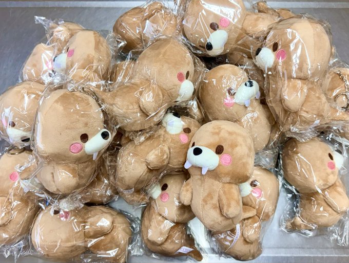 A pile of individually plastic-wrapped plush toys shaped like brown, round creatures with small white faces, pink cheeks, and tiny fangs.