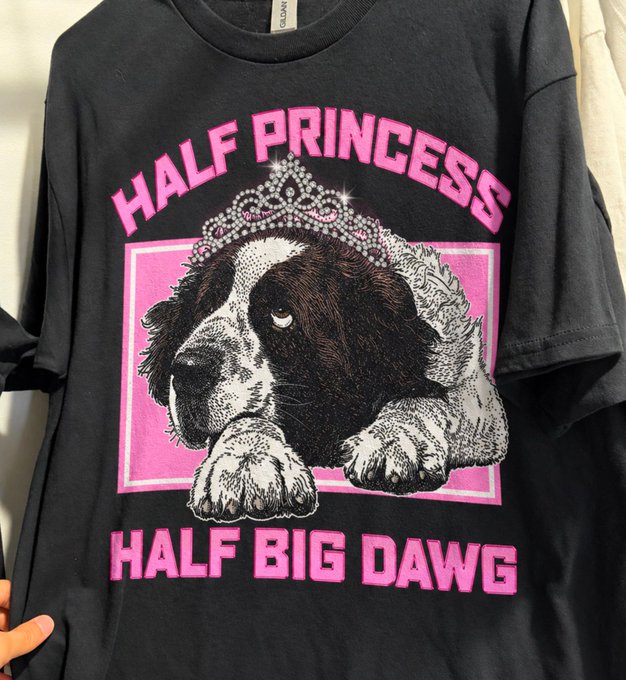 A black t-shirt with a pink graphic featuring a Saint Bernard dog wearing a tiara, with the text 'HALF PRINCESS' above and 'HALF BIG DAWG' below.