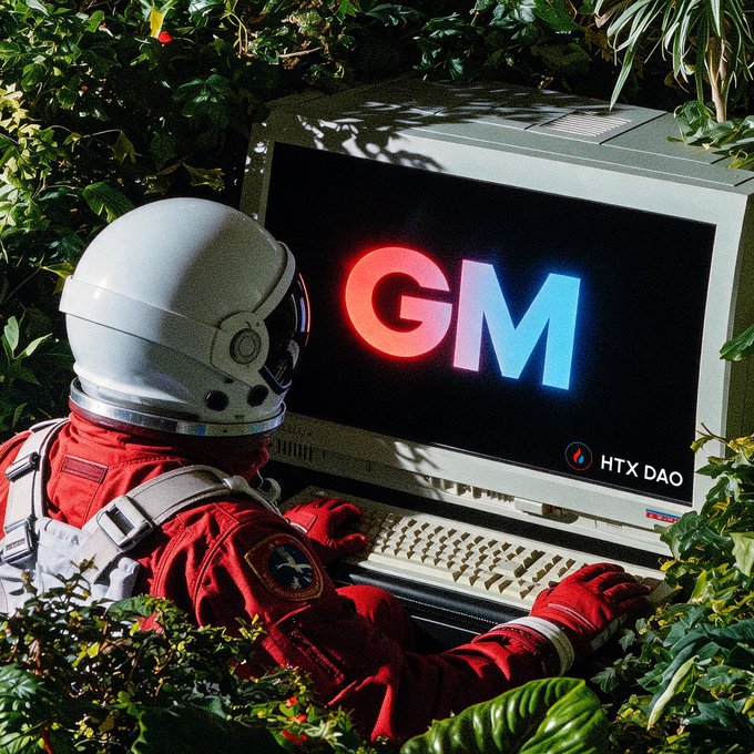 An astronaut in a red spacesuit and white helmet types on a vintage computer displaying the glowing 'GM' logo and 'HTX DAO' in a jungle setting.