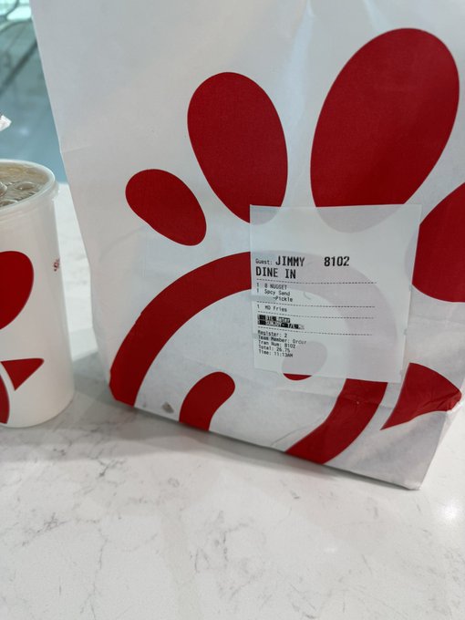 A Chick-fil-A paper bag with a drink cup sits on a marble counter, displaying an order label for 'JIMMY' (order 8102, Dine In).