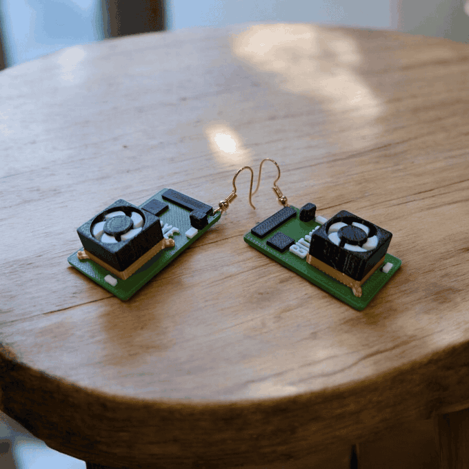 A pair of earrings designed to look like miniature computer RAM sticks with small cooling fans, displayed on a round wooden surface.