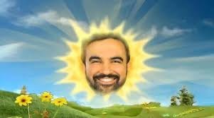A photoshopped image of a man's smiling face superimposed onto a stylized sun with sun rays, set against a backdrop of a green meadow with sunflowers and a blue sky.