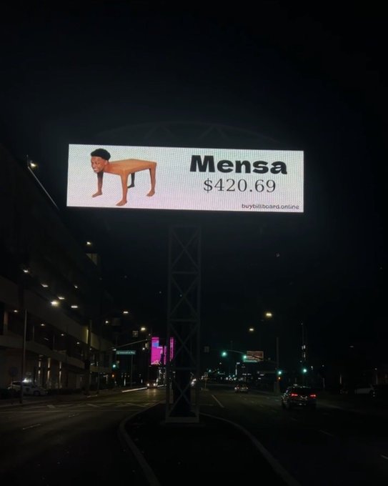 An illuminated billboard at night above a city street advertising 'Mensa' for '$420.69' with the text 'buybitboard.online' and an image of a person doing a pushup.