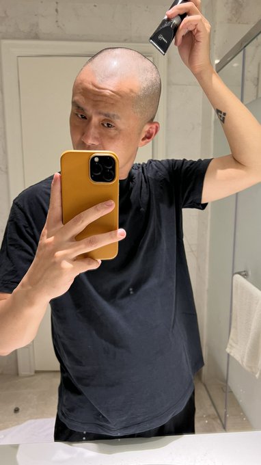 A man takes a mirror selfie in a bathroom while holding clippers near his freshly shaved head, humorously illustrating his post about going bald if any BNBChain token flips a 300M market cap.