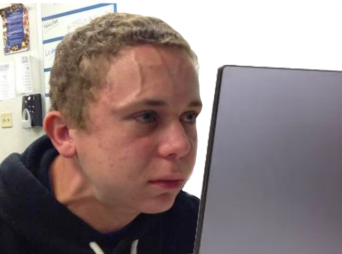 A close-up of a young man with short blonde hair staring intently at a laptop screen in what appears to be a classroom or office setting.