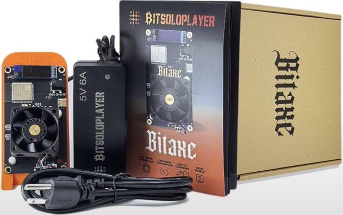 A Bitaxe Solo Player Bitcoin mining device with its power supply (5V 6A) and packaging box, featuring a circuit board with a cooling fan and a US power cord.