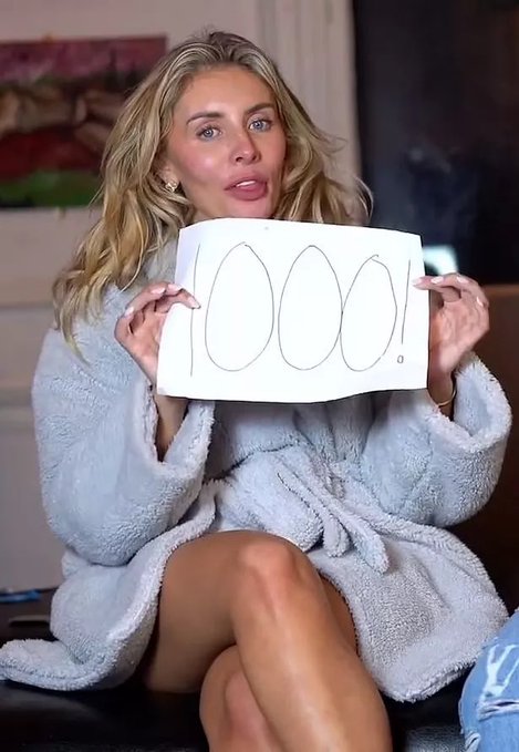 In the image, a woman wearing a robe or bathrobe is sitting on a couch with her legs crossed. She holds up a piece of paper containing a drawing of 100 white eggs against a black background. The caption at the bottom of the picture states "The price of ETH in a couple days".