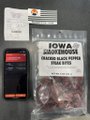A product photo showing what appears to be a novelty item package labeled 'IOWA SHOWER HOSE' alongside other small packaged items on a dark surface.