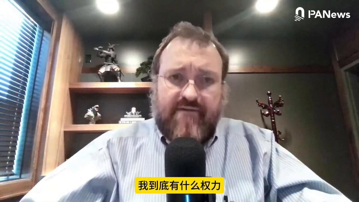 The image shows a man wearing glasses sitting at a desk with a microphone, likely participating in an online interview or webinar. The background features a window that allows natural light into the room. The caption of the image reads "Cardano 创始人摊牌：$ADA 生态下半年要过苦日子了 Cardano 创始人 Charles Hoskinson 在视频中表示", which is related to the post about the man named Charles Hoskinson.