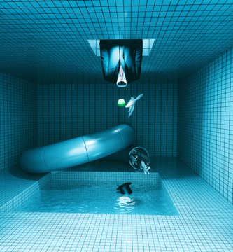 A surreal 3D render of a tiled blue pool room containing a large cylindrical capsule and a floating figure, with a person partially submerged in the pool water below.