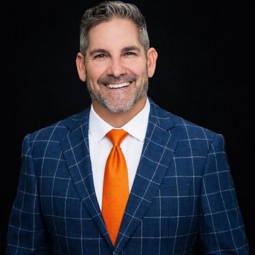 A professional headshot of Grant Cardone, a billionaire real estate investor, smiling in a blue checkered suit and bright orange tie. The image accompanies his statement about Cardone Capital's strategy to acquire more Bitcoin as its price declines.