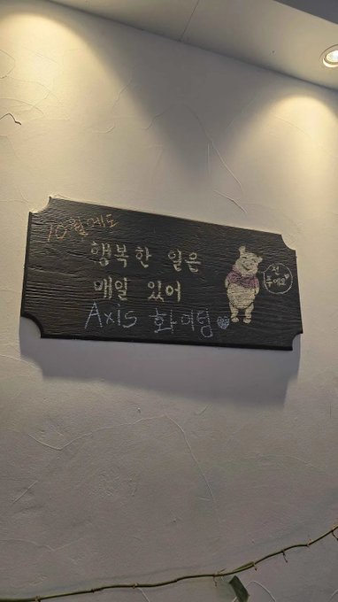 A black wooden sign mounted on a wall with Korean writing and a drawing of a sheep, celebrating a 10th birthday and naming the person as 'Axis' class representative.
