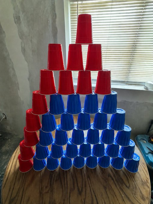 A pyramid of stacked red and blue Solo cups with red arranged in a bull-like shape on a wooden table, fitting the "gm" (good morning) and bullish tone of the post.
