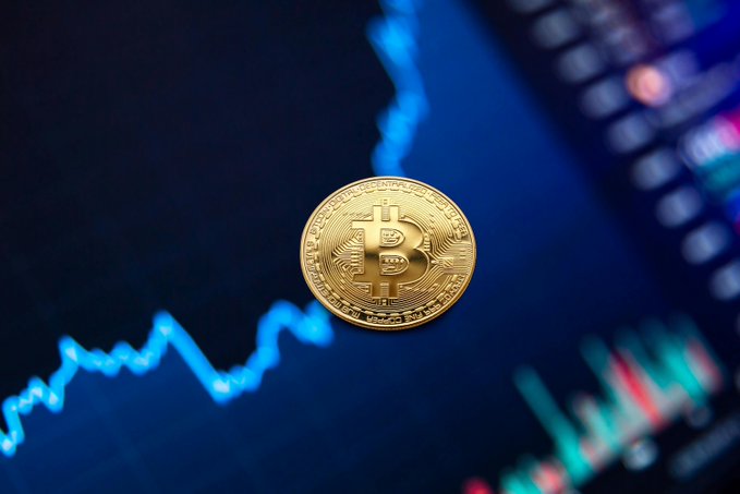 A physical Bitcoin token rests atop a digital trading chart displaying a rising price trend with candlestick patterns in the background, visually reinforcing the surge in global BTC ETP inflows highlighted in the caption.